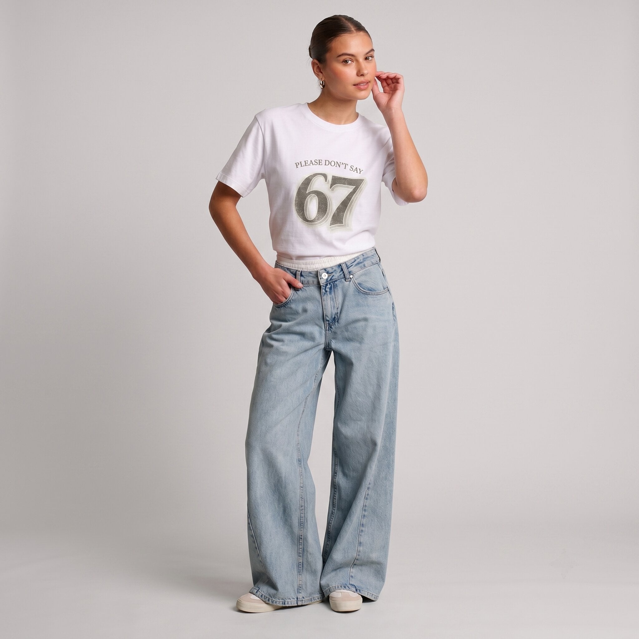 Woman wearing Kiksy white relaxed slogan t-shirt featuring Please Don't Say 67 print with casual blue jeans.