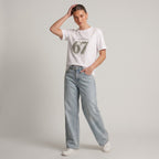 Woman wearing Kiksy white relaxed slogan t-shirt featuring Please Don't Say 67 print with casual blue jeans.
