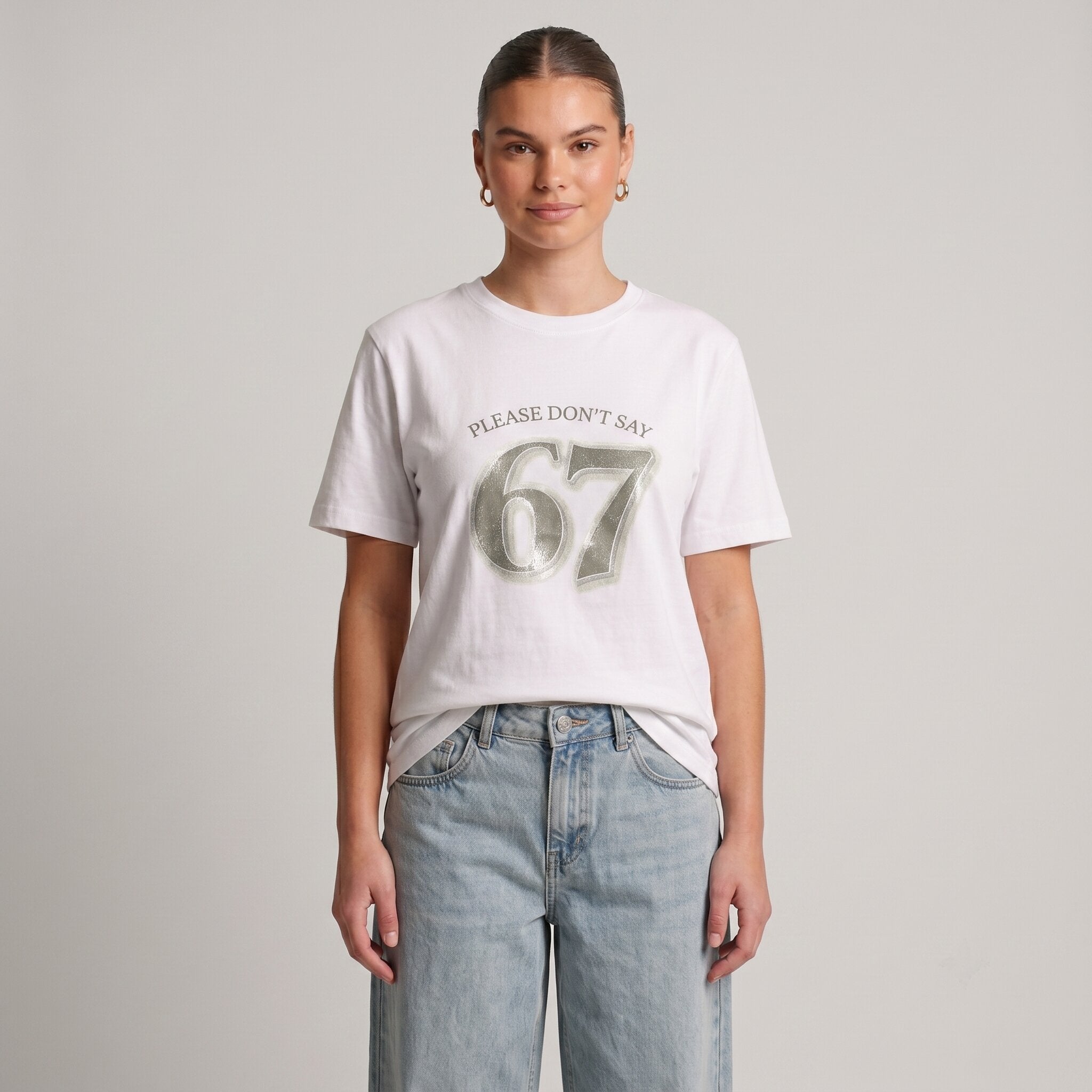 Woman wearing Kiksy white relaxed slogan t-shirt featuring Please Don't Say 67 print with casual blue jeans.