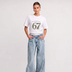 Woman wearing Kiksy white relaxed slogan t-shirt featuring Please Don't Say 67 print with casual blue jeans.
