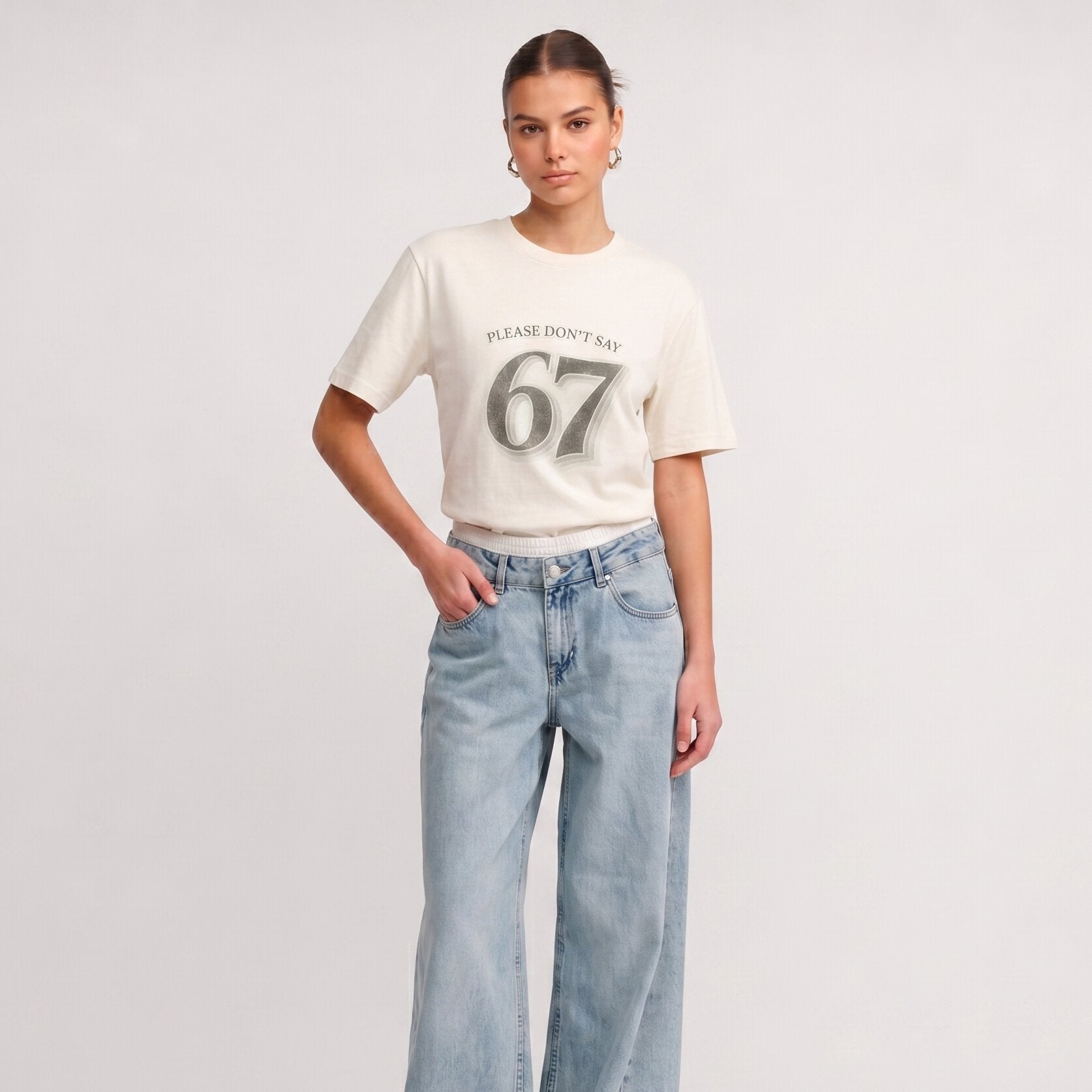 Woman wearing Kiksy white relaxed slogan t-shirt featuring Please Don't Say 67 print with casual blue jeans.