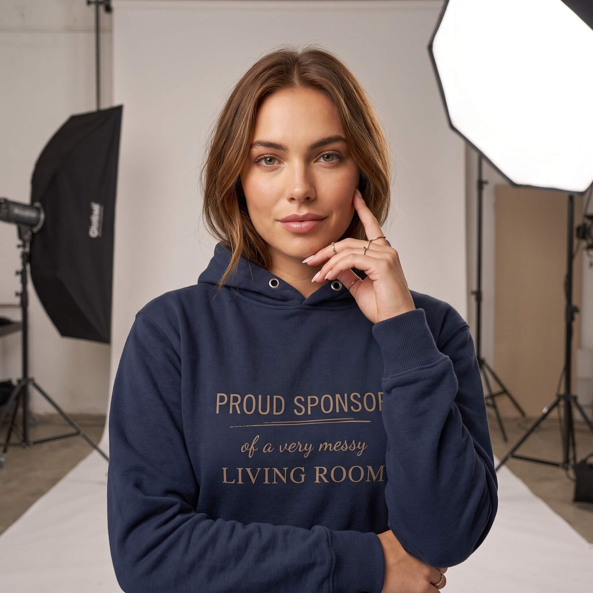 Woman wearing Kiksy dark blue hoodie featuring the text Proud Sponsor of a very messy LIVING ROOM