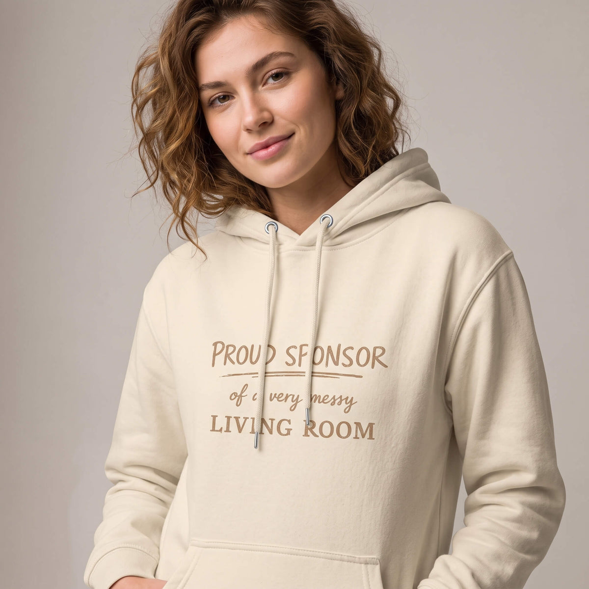 Woman wearing Kiksy nude hoodie featuring the text Proud Sponsor of a very messy LIVING ROOM