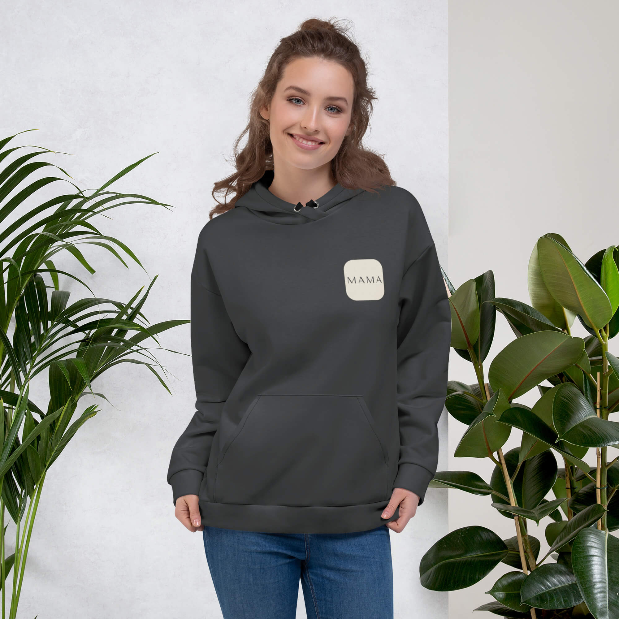 Woman smiling in a Kiksy charcoal grey hoodie featuring a cream square MAMA chest logo.