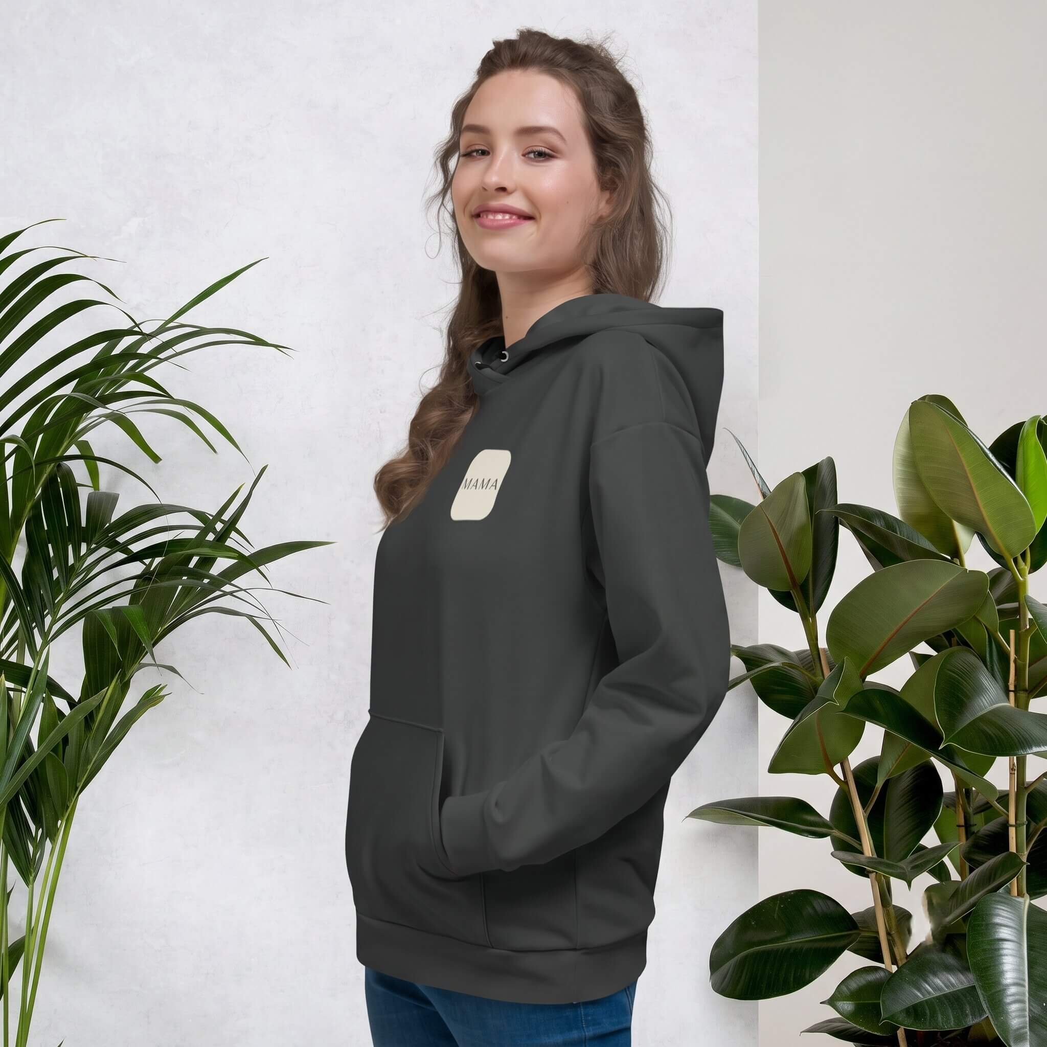 Woman smiling in a Kiksy charcoal grey hoodie featuring a cream square MAMA chest logo.
